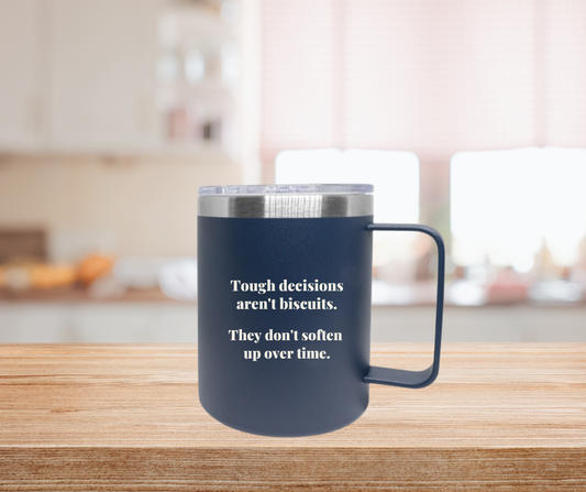 A blue cup with a silver rim and clear lid with the words Tough decisions aren't biscuits. They don't soften up over time on a kitchen counter top