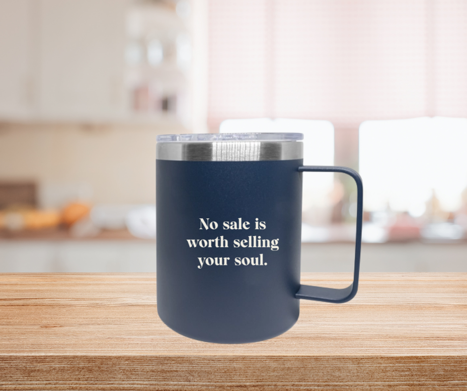 A blue cup with a silver rim and clear lid with the words No sale is worth selling your soul on a kitchen counter top